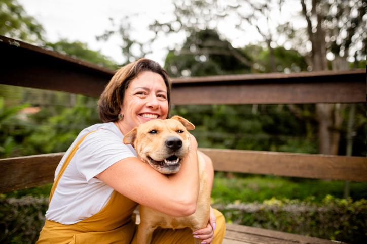 miling mature woman giving her cog a big hug while sitting together outside on her patio in her back yard